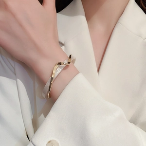 Close-up of gold-plated wavy open bangle with white marble texture on model's wrist