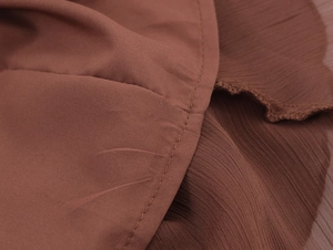 Close-up of brown chiffon fabric showing delicate ruffled edges and fine stitching details