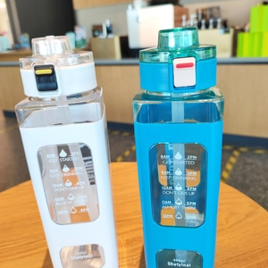 Close-up of 900ml square plastic bottles with time markers and straws on a wooden table