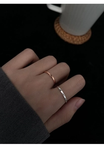 Close-up of slim silver and rose gold adjustable rings worn on a hand against a black background