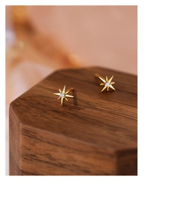 Macro shot of gold S999 silver eight-pointed star stud earrings with zircon on wood