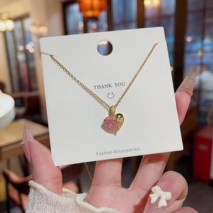 Détail macro du pendentif cœur en zircon rose avec finition dorée sur carte de présentation