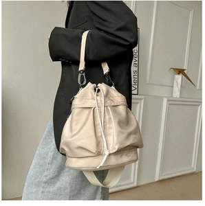 Detail of beige nylon drawstring bucket bag with adjustable shoulder strap worn by model