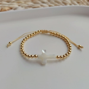 Close-up of gold beaded bracelet featuring a white shell cross charm and adjustable cord