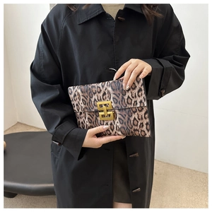 Leopard print clutch bag with gold square buckle shown held by a model in a minimal setting