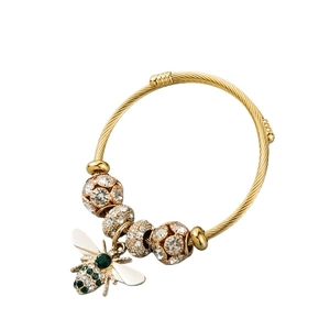 Close-up of golden bee pendant with green gemstone eye and pavé crystal ball accents