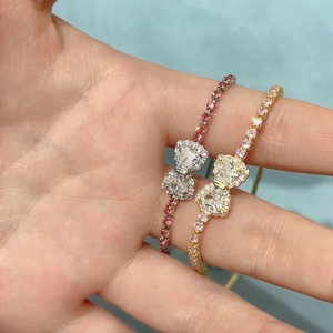 Detailed view of silver and gold bow bracelets with zircon inlay on a blue textured background