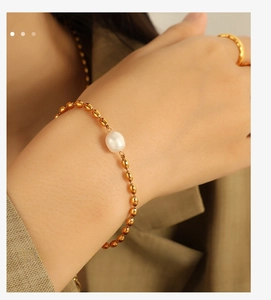 Close-up of a minimalist gold beaded bracelet featuring a white pearl on a woman's wrist