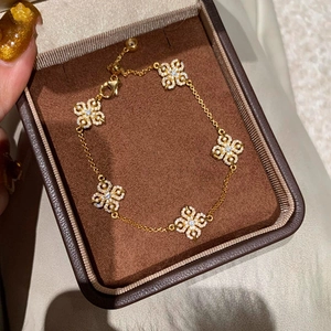 Macro detail of a 14k gold plated bracelet with five clover pendants in a velvet box
