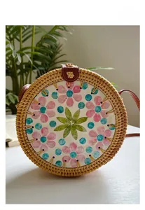 Close-up of a round rattan bag featuring a colorful floral shell inlay and leather clasp