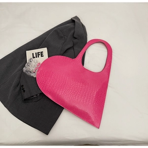 Detailed view of pink heart-shaped bag with crocodile texture and fashion lifestyle props