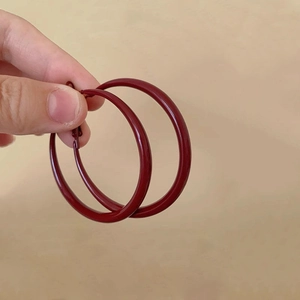 Macro shot of large burgundy red enamel hoop earrings held by hand for scale