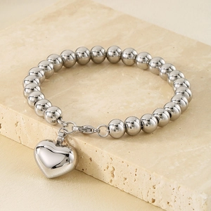 Détail d'un bracelet à billes argenté avec pendentif cœur 3D sur une surface en pierre