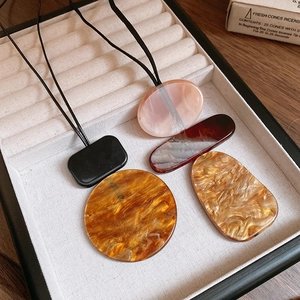 Close-up of geometric resin pendants in amber and marble textures on a white jewelry tray