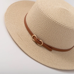 Detailed view of beige paper woven sun hat with brown leather strap and gold buckle detail