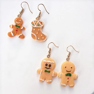 Detail of handmade asymmetric gingerbread man and Christmas sock earrings on white background