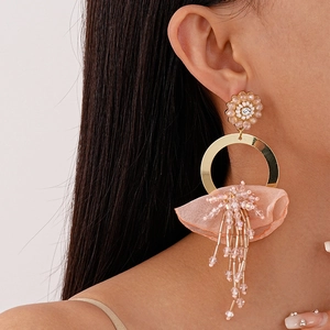 Detail of lace flower earrings with pink tassels and gold ring on a model's ear