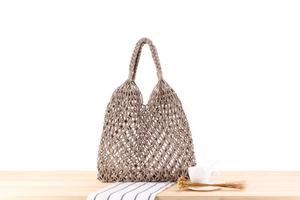 Detailed close-up of khaki hand-woven mesh tote bag with spiral handles on wood surface