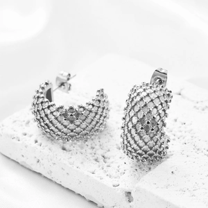 Detailed view of silver mesh C-shaped earrings with lattice texture on a stone base