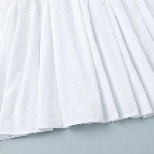 Vue détaillée du tissu plissé blanc et de l'ourlet raffiné sur la mini robe d'été