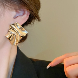 Close-up of a gold-plated irregular pleated earring worn by a model in warm light