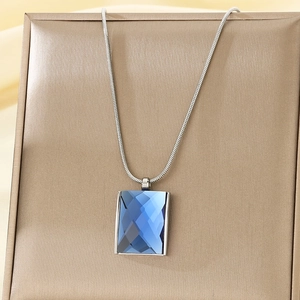 Detail of blue rectangular crystal pendant on silver snake chain displayed on a gold stand