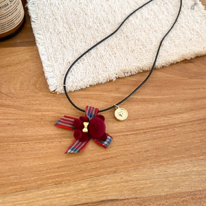 Primo piano di una collana con orsetto bordeaux e fiocco scozzese su tavolo in legno