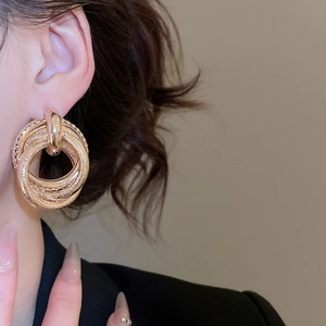 Close-up of layered gold metal hoop earrings with mixed textures on a female model