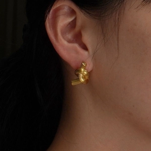 Golden knotted stud earrings in polished stainless steel shown on model