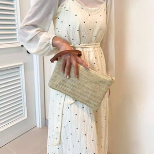 Fashionable beige straw clutch bag with brown leather wristlet held by a model
