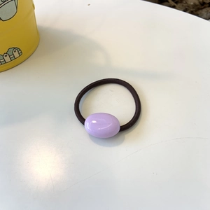 Detail view of purple oval bead hair tie with elastic black rope on white surface