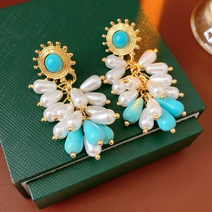 Detailed close-up of vintage gold tassel earrings with pearls and turquoise on jewelry box