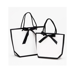 Detail of white gift bags with black trim and elegant ribbon bows in two sizes