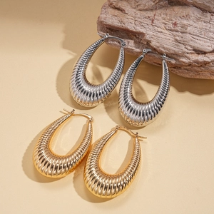 Textured gold and silver chunky teardrop hoop earrings on a beige minimalist background