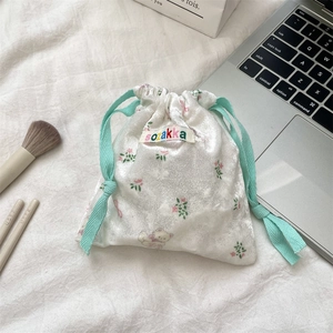 Detail of white velvet drawstring bag with bear and floral prints next to brushes