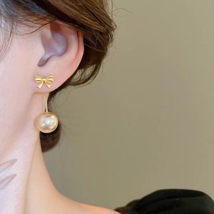 Detailed close-up of bow knot pearl earrings on a model with a subtle champagne pearl drop