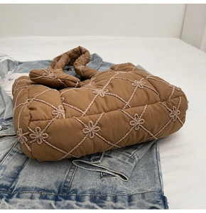 Macro view of brown quilted puffer tote bag featuring delicate white floral embroidery