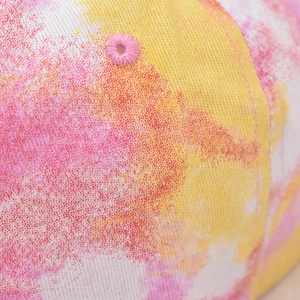 Macro shot of pink and yellow tie-dye fabric with glitter and embroidered eyelet detail