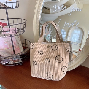 Close-up of beige corduroy tote bag with black smiley patterns on a wooden table