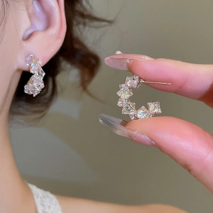 Macro shot of geometric C-shaped gold earrings with square-cut pink zircon crystals
