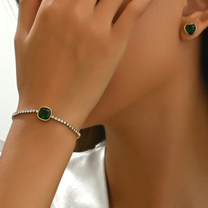 Detalle de una pulsera dorada con esmeralda cuadrada y pendientes en forma de corazón