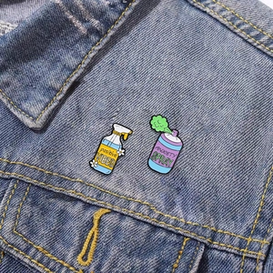 Detail showing positive vibes and anxiety spray enamel pins on a denim jacket