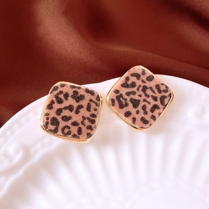 Close-up of leopard print square studs on a white vintage plate with brown silk background