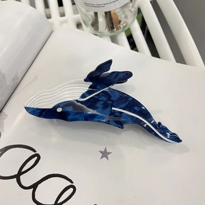 Macro shot of whale-shaped acetate hair claw clip with blue marble texture on a book