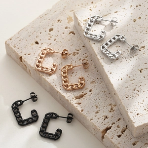Macro shot of silver, rose gold, and black Cuban chain hoop earrings on textured stone