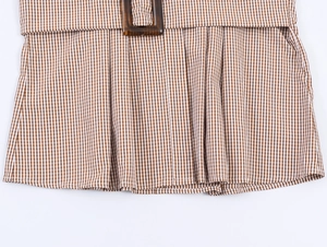 Detail von braunem Karohemdkleid mit bernsteinfarbener Gürtelschnalle und Falten
