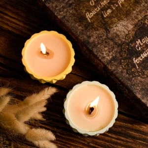 Detail of lit scented candles with wavy edges in pastel yellow and cyan on vintage wood
