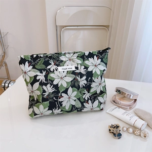 Floral canvas makeup bag with zipper and woven label surrounded by beauty accessories