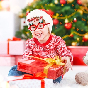 Enfant portant des lunettes de Noël rouges HO HO HO festives dans un décor chaleureux de fête