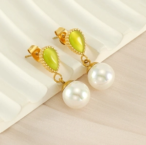 Détail de boucles d'oreilles dorées avec pierre œil de chat verte et perle ronde blanche